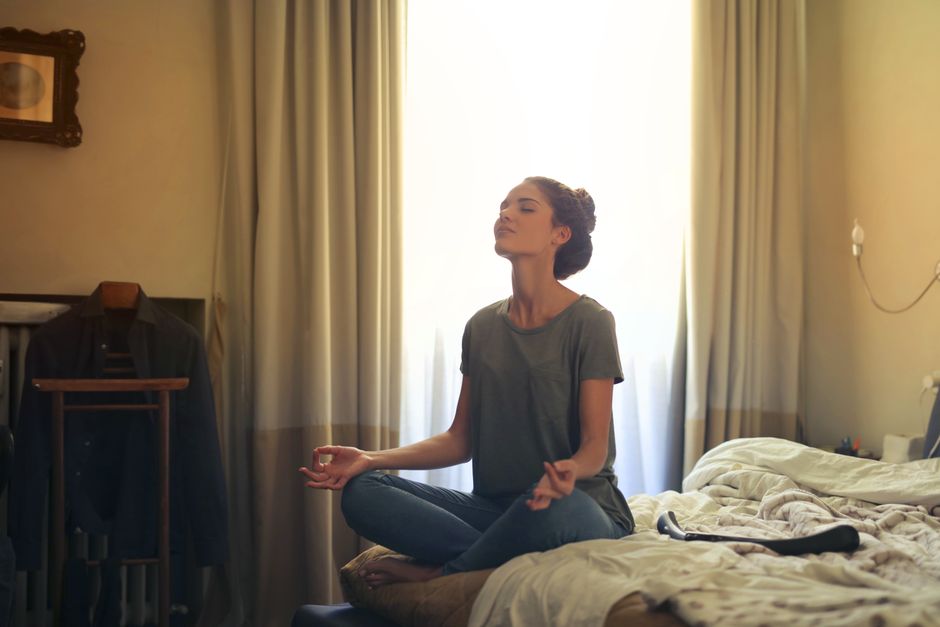 Mulher meditando sentada em uma almofada com os olhos fechados e expressão serena